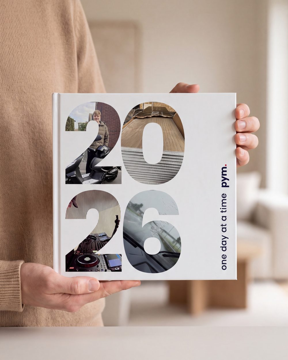 Two hands holding a printed PYM 2026 yearbook, the year set in photographs