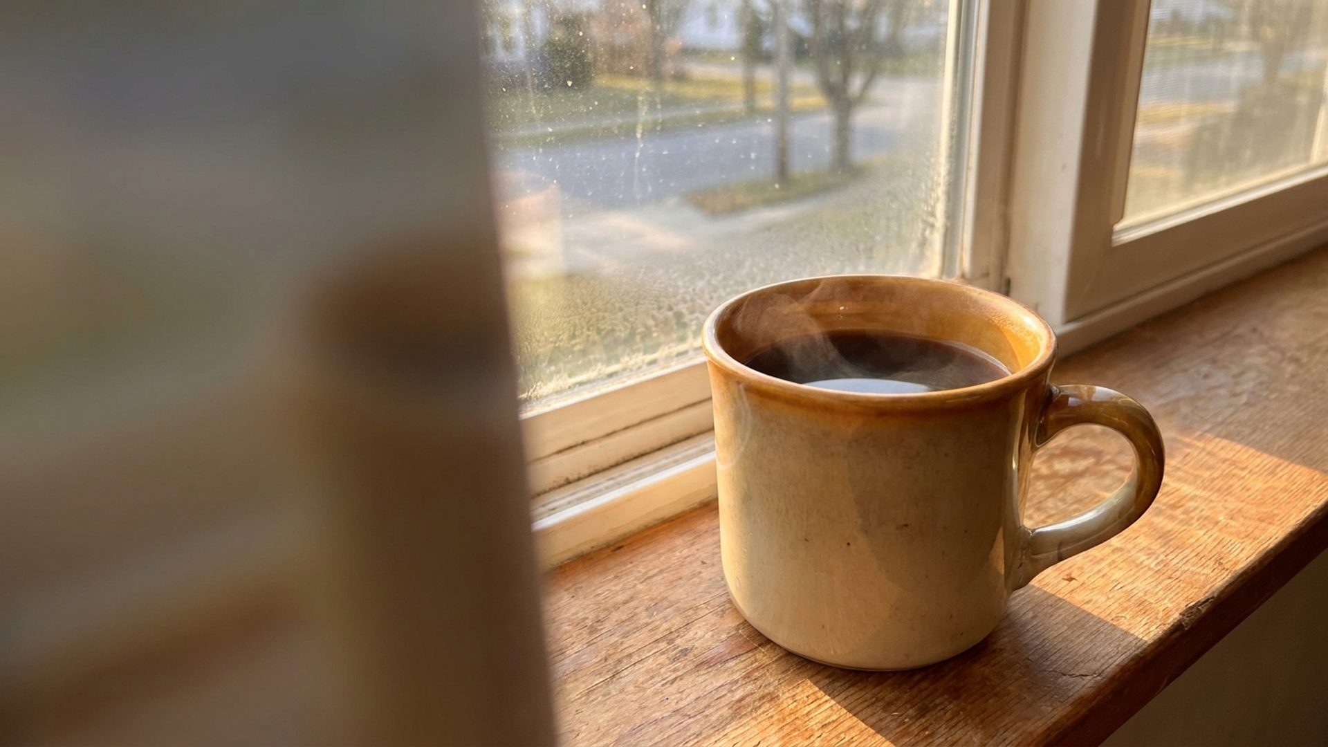 A mug of coffee steaming on a window sill in morning light, one day of a year